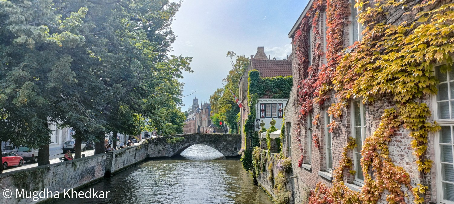 A canal in Bruges with a stone bridge and ivy-covered houses in autumn