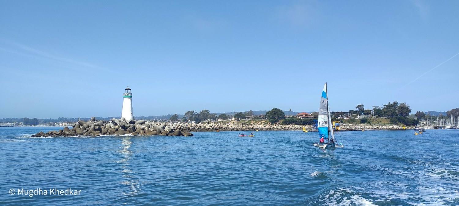 A white lighthouse on a rocky jetty as a boat sets out into Monterey Bay