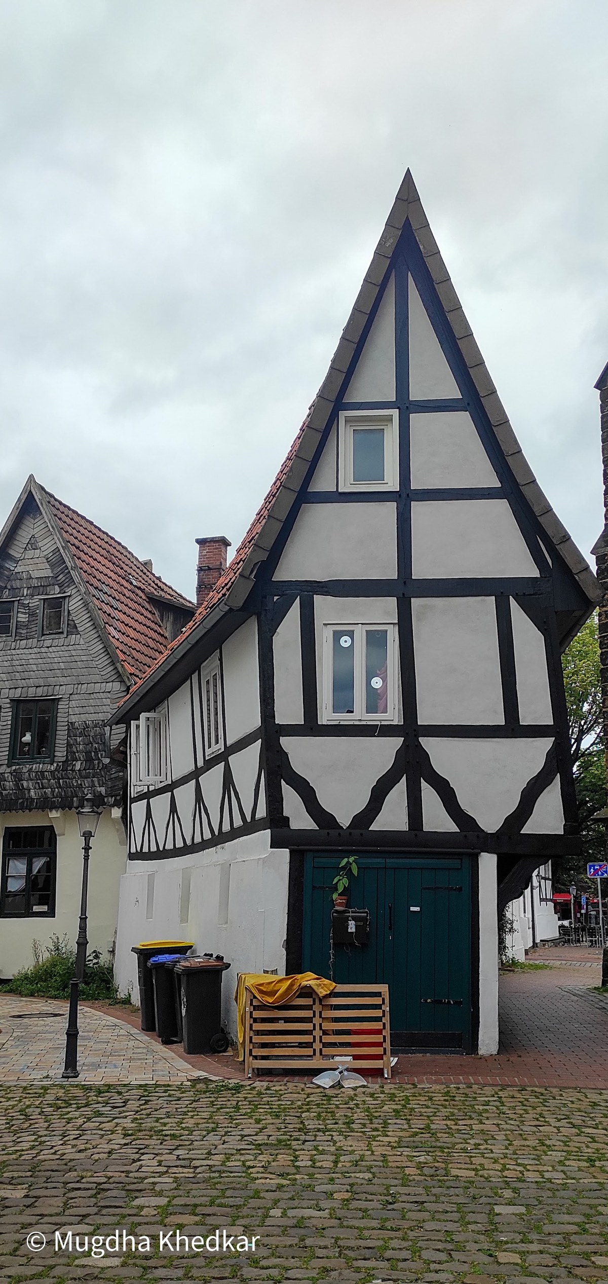 A narrow half-timbered house with a steep gable on a cobbled street in Minden