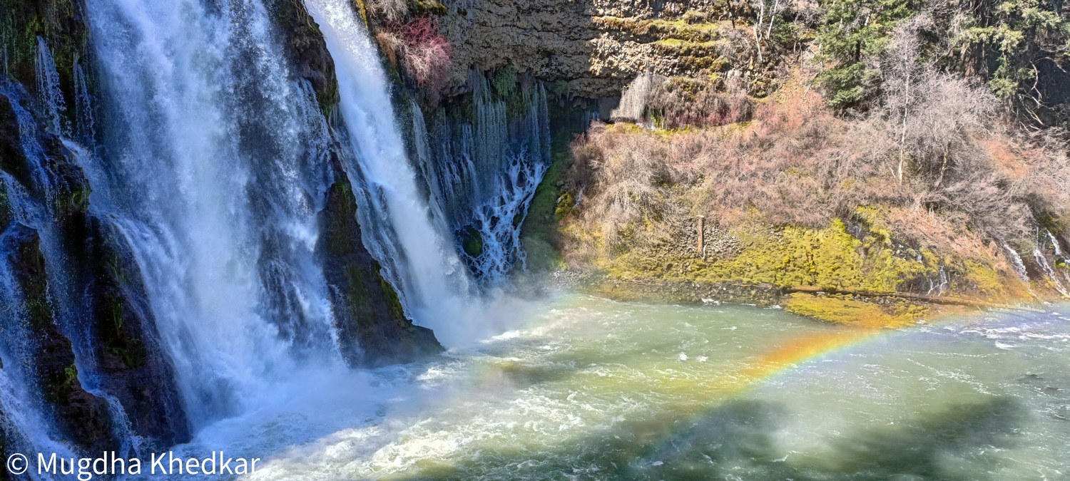 Burney Falls pouring over a mossy cliff, with a rainbow in the spray